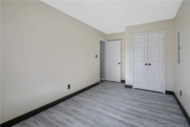 unfurnished bedroom with electric panel, light wood-type flooring, and a closet