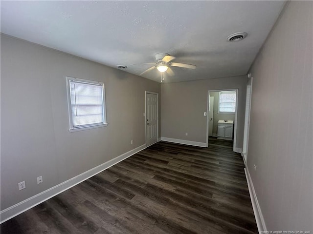 empty room featuring ceiling fan, a healthy amount of sunlight, and dark wood-type flooring