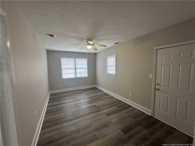 spare room featuring ceiling fan, dark wood-type flooring, and wood walls