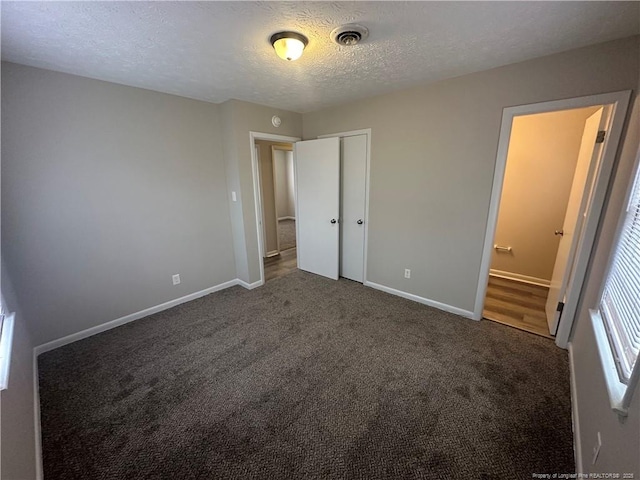 unfurnished bedroom with a textured ceiling, dark colored carpet, and a closet