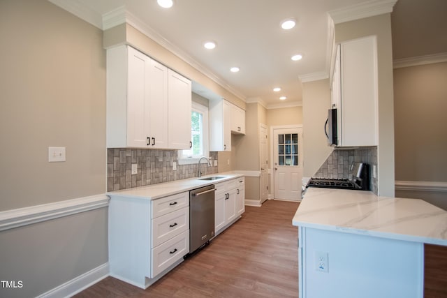 kitchen featuring stainless steel appliances, kitchen peninsula, light stone countertops, sink, and white cabinetry