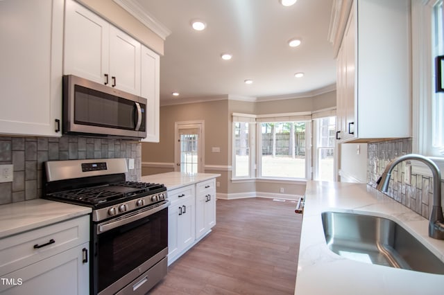 kitchen featuring stainless steel appliances, white cabinetry, sink, and light stone counters