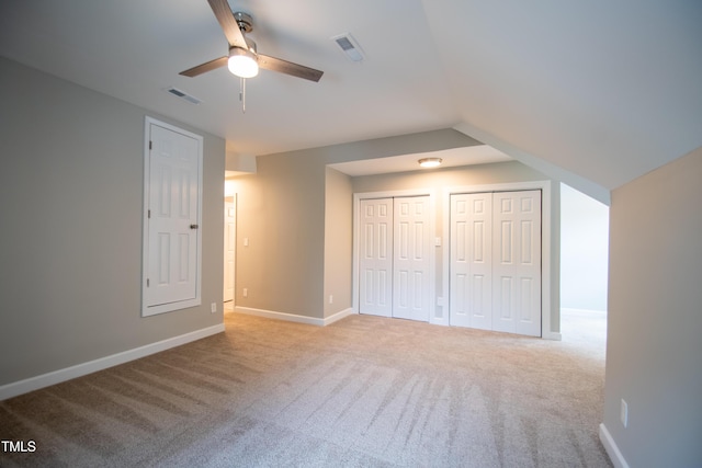 unfurnished bedroom with ceiling fan, multiple closets, vaulted ceiling, and light carpet