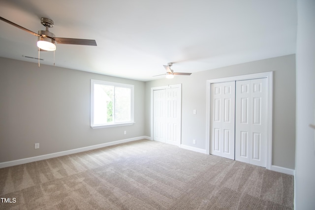 unfurnished bedroom featuring two closets, ceiling fan, and light carpet