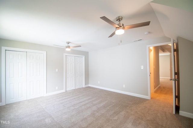 unfurnished bedroom with vaulted ceiling, two closets, ceiling fan, and light carpet