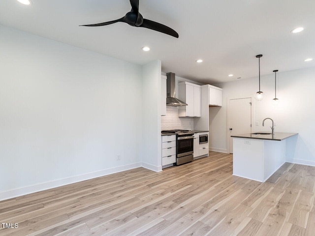 kitchen featuring hanging light fixtures, stainless steel appliances, wall chimney range hood, white cabinets, and sink