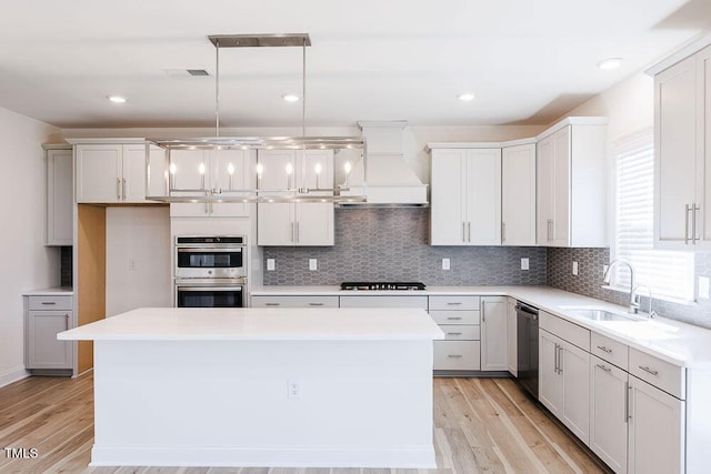 kitchen featuring sink, decorative light fixtures, gas cooktop, stainless steel double oven, and a kitchen island