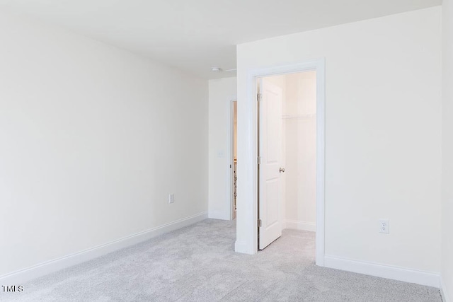 unfurnished bedroom featuring a walk in closet, a closet, and light carpet