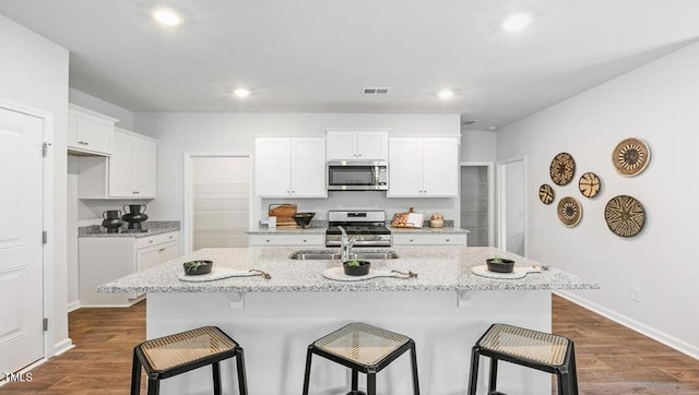 kitchen with a center island with sink, white cabinets, appliances with stainless steel finishes, a kitchen breakfast bar, and sink