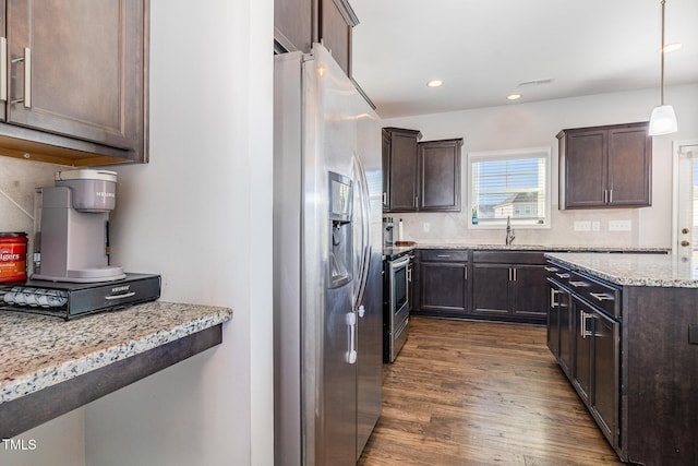 kitchen featuring appliances with stainless steel finishes, light stone counters, backsplash, hanging light fixtures, and dark wood-type flooring