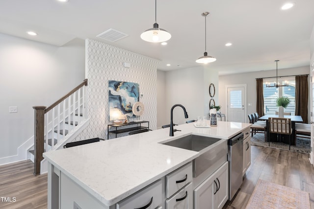 kitchen featuring light stone countertops, dishwasher, hanging light fixtures, a kitchen island with sink, and sink