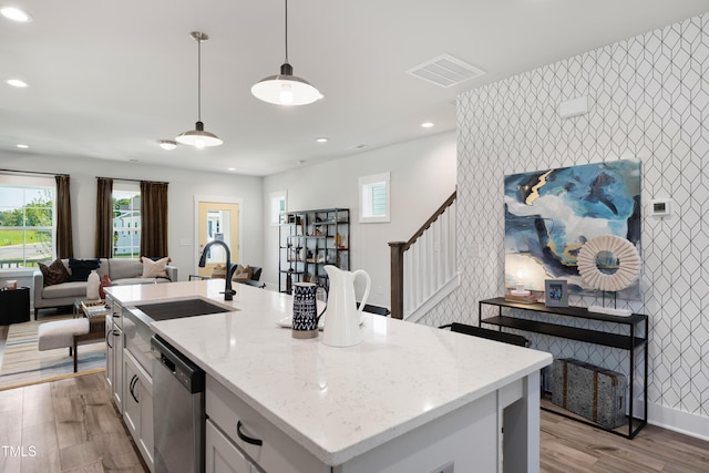 kitchen featuring stainless steel dishwasher, light wood-type flooring, a kitchen island with sink, and hanging light fixtures