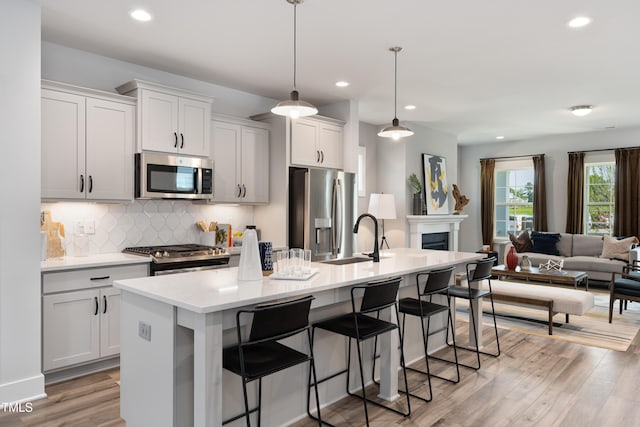 kitchen with a kitchen island with sink, stainless steel appliances, pendant lighting, decorative backsplash, and sink