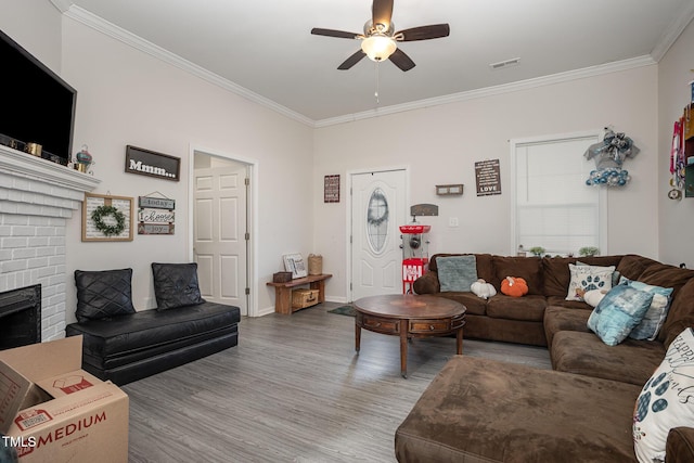 living room featuring ceiling fan, light wood-type flooring, ornamental molding, and a fireplace