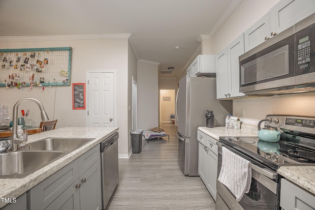 kitchen with light stone countertops, light hardwood / wood-style flooring, crown molding, appliances with stainless steel finishes, and sink