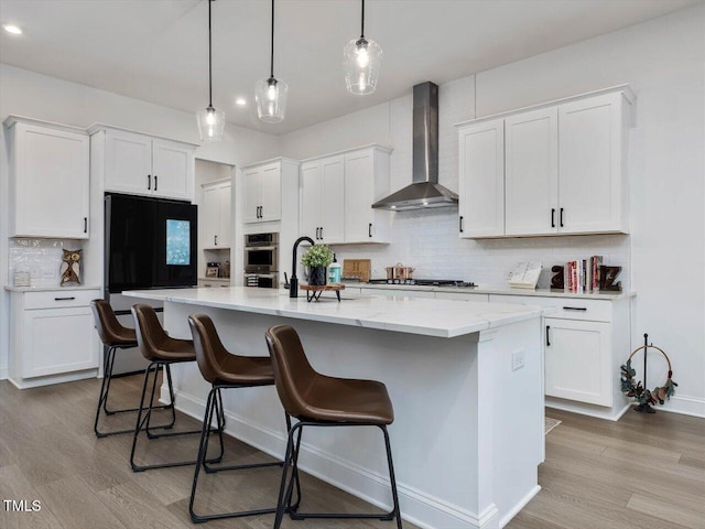 kitchen with decorative light fixtures, white cabinets, wall chimney exhaust hood, decorative backsplash, and a center island with sink