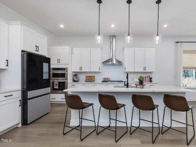 kitchen featuring wall chimney range hood, an island with sink, and appliances with stainless steel finishes