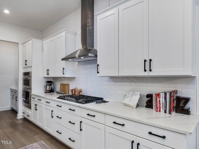 kitchen with stainless steel appliances, white cabinets, light stone counters, wall chimney exhaust hood, and dark wood-type flooring