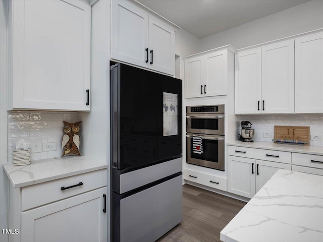 kitchen with light stone countertops, stainless steel double oven, dark hardwood / wood-style floors, white cabinets, and tasteful backsplash