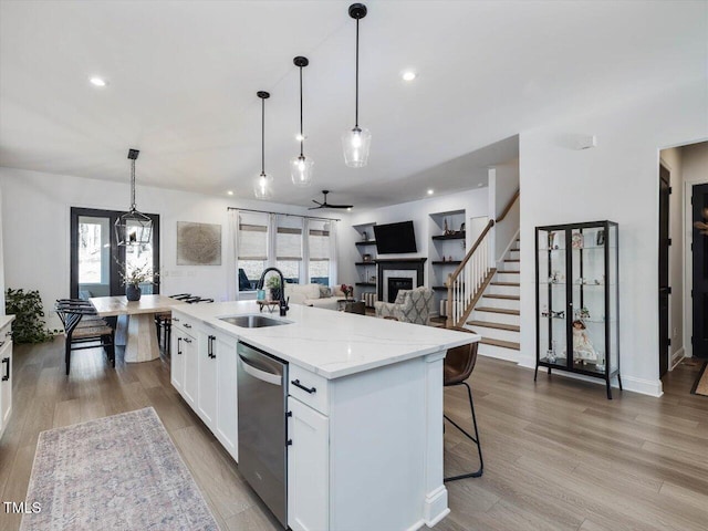 kitchen with an island with sink, sink, white cabinetry, decorative light fixtures, and stainless steel dishwasher