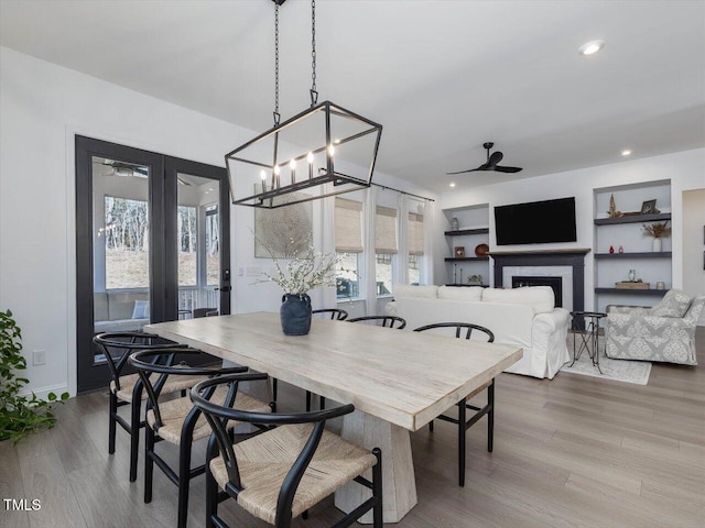 dining room featuring ceiling fan with notable chandelier, light wood-type flooring, and built in shelves