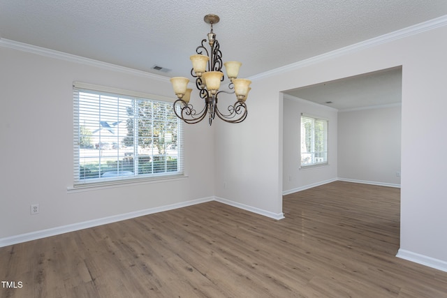 spare room with a wealth of natural light, wood-type flooring, ornamental molding, and a notable chandelier