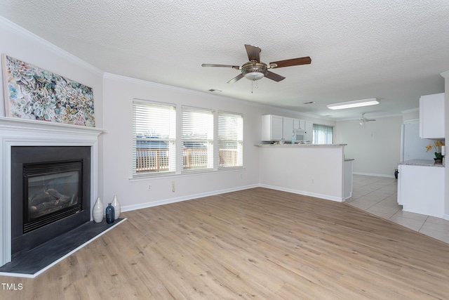 unfurnished living room with ceiling fan, a textured ceiling, ornamental molding, and light wood-type flooring