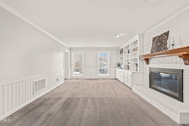 unfurnished living room featuring crown molding, a brick fireplace, built in shelves, and light colored carpet