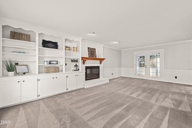 unfurnished living room featuring a fireplace, ornamental molding, light carpet, built in shelves, and french doors