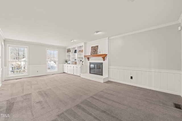 unfurnished living room featuring crown molding, built in shelves, a fireplace, and carpet