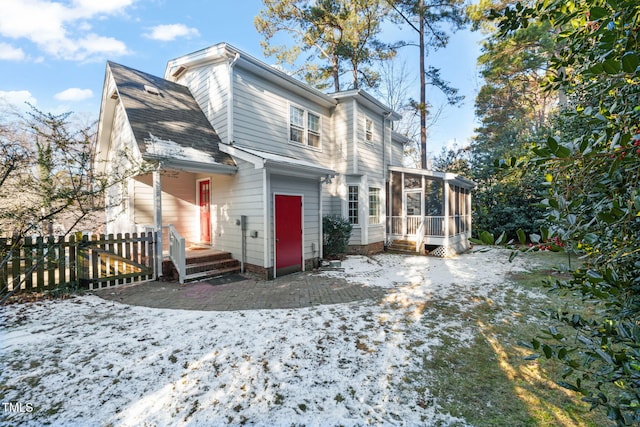 snow covered property with a garage and a sunroom