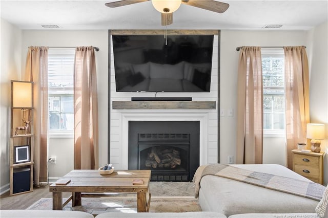 living room with a large fireplace, light wood-type flooring, and ceiling fan