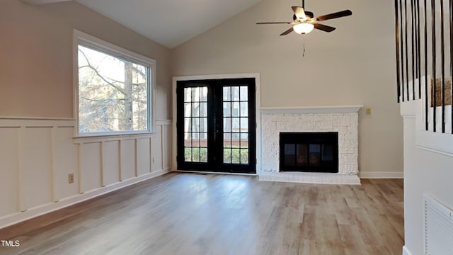 unfurnished living room with a healthy amount of sunlight, french doors, a fireplace, light hardwood / wood-style flooring, and lofted ceiling