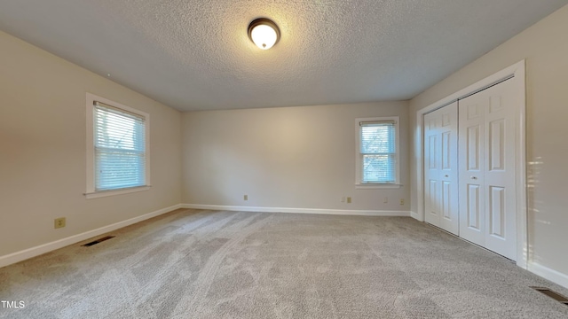 unfurnished bedroom with a textured ceiling, light carpet, and multiple windows