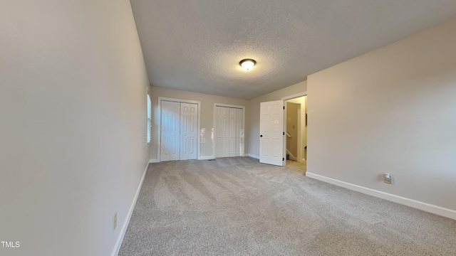 unfurnished bedroom with a textured ceiling, multiple closets, and light carpet