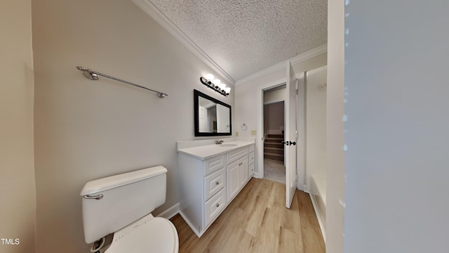 bathroom featuring wood-type flooring, toilet, crown molding, vanity, and a textured ceiling