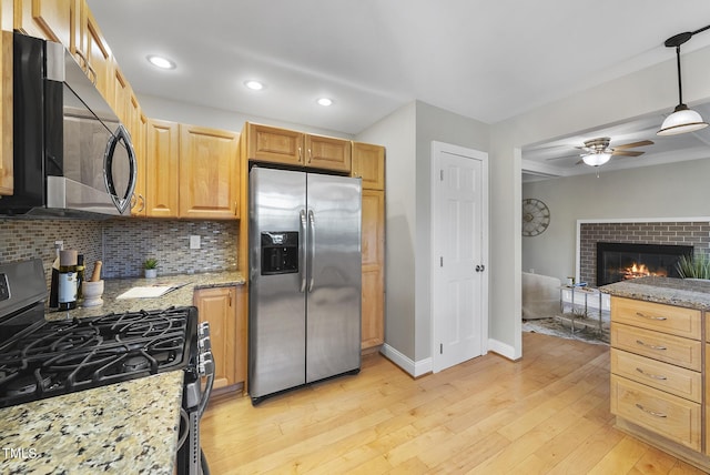 kitchen featuring a brick fireplace, stainless steel refrigerator with ice dispenser, light wood-type flooring, light stone countertops, and gas range oven