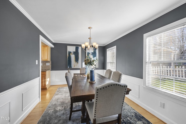 dining area with light hardwood / wood-style floors, ornamental molding, and a chandelier