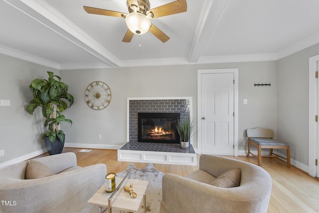 living room featuring a brick fireplace, ceiling fan, ornamental molding, beam ceiling, and light hardwood / wood-style flooring