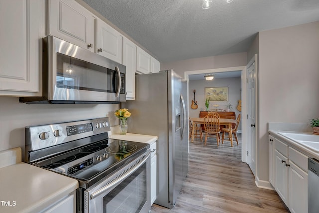 kitchen with a textured ceiling, white cabinets, appliances with stainless steel finishes, sink, and light hardwood / wood-style flooring