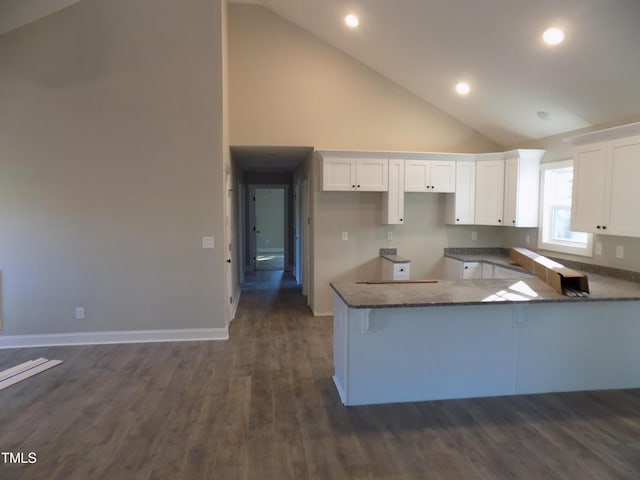 kitchen with white cabinetry, dark stone countertops, kitchen peninsula, high vaulted ceiling, and dark hardwood / wood-style flooring