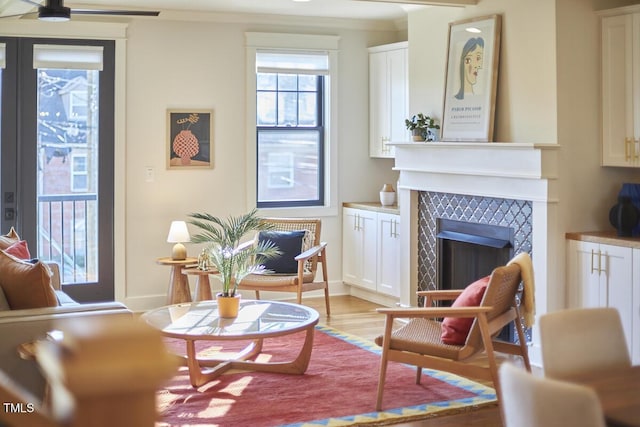 living area featuring a tiled fireplace, ornamental molding, and light hardwood / wood-style flooring