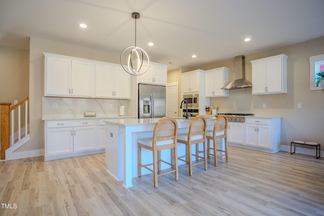 kitchen featuring wall chimney range hood, built in appliances, white cabinetry, and light hardwood / wood-style flooring