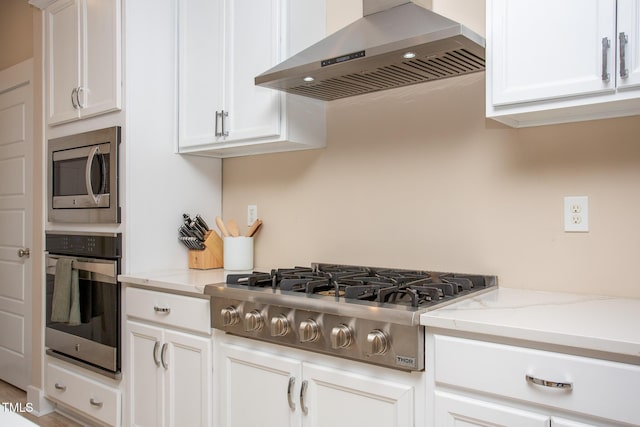 kitchen featuring light stone countertops, white cabinets, appliances with stainless steel finishes, and extractor fan