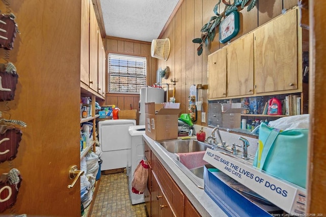 interior space featuring electric water heater, wood walls, a textured ceiling, sink, and washing machine and clothes dryer