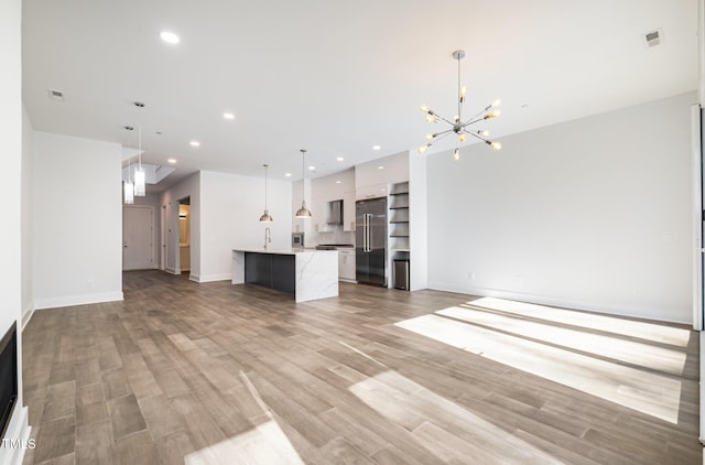 unfurnished living room with an inviting chandelier, light hardwood / wood-style floors, and sink