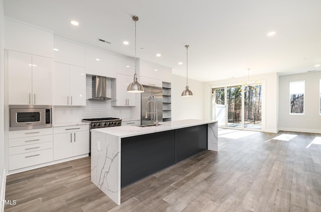 kitchen featuring built in appliances, white cabinets, a kitchen island with sink, and wall chimney exhaust hood