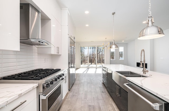 kitchen with decorative light fixtures, white cabinets, wall chimney range hood, and premium appliances