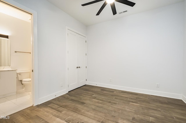 unfurnished bedroom with ceiling fan, dark wood-type flooring, and ensuite bathroom