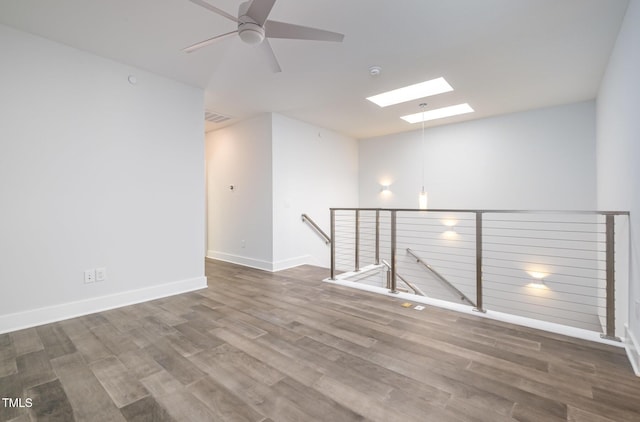 spare room with ceiling fan, a skylight, and hardwood / wood-style flooring